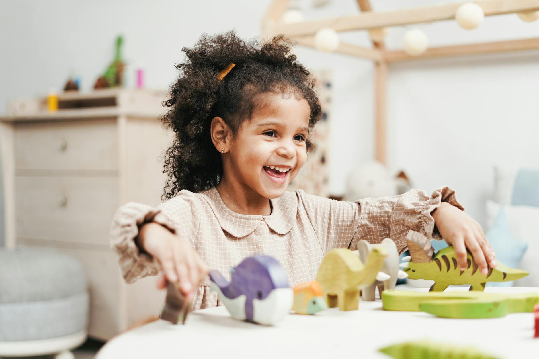 selective focus photo of laughing young girl playing with wooden toys on white table